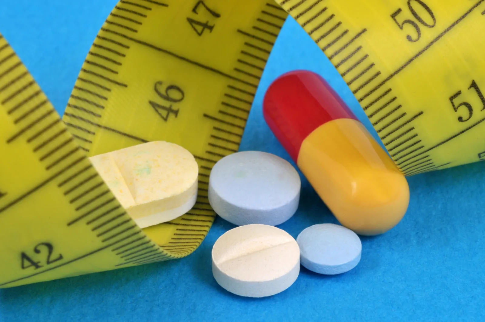 Tabletten und eine Kapsel neben einem gelben Maßband auf blauem Untergrund