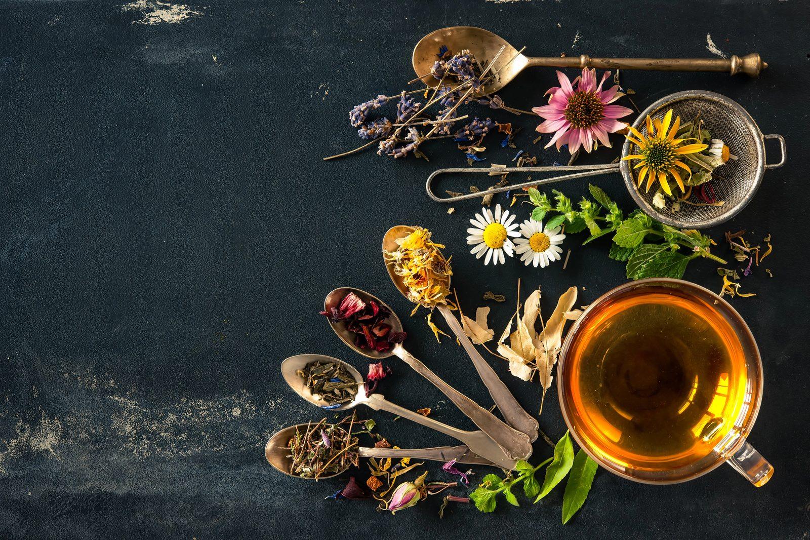 Kräutertee mit getrockneten Blüten, Teesieb und Löffeln auf dunklem Untergrund – Ketose beim Fasten